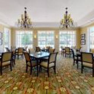 An elegant dining room with several tables and chairs, featuring chandeliers and large windows.