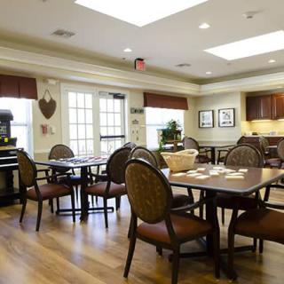A cozy dining area with tables and chairs, featuring a wooden floor and a small kitchen space in the background.