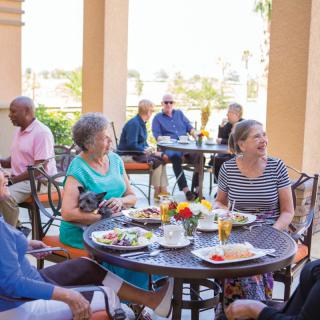A group of seniors enjoying a meal and conversation at an outdoor restaurant.