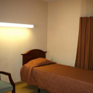 A simple hotel room with a single bed, chair, and curtain under soft lighting.