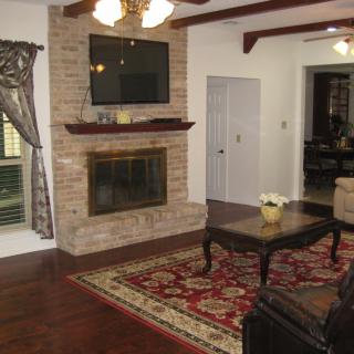 A cozy living room featuring a stone fireplace with a mounted TV above, a coffee table on an ornate rug, and wooden floors.