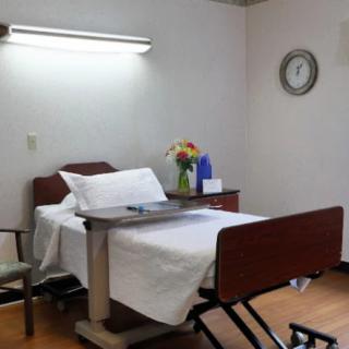 A hospital room with a bed, bedside table, and flowers.