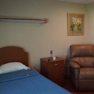 A simple hospital room with a bed, armchair, and wall art.