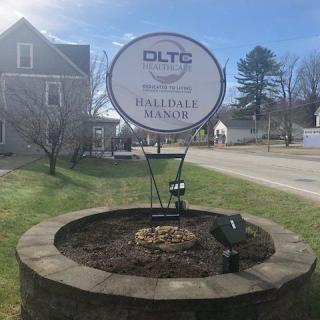 An outdoor sign for Hillside Manor surrounded by a grass lawn and adjacent to a road.
