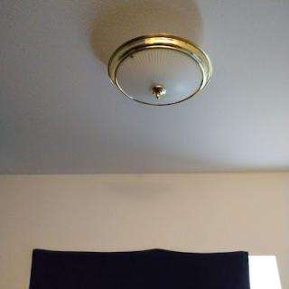 A view of a ceiling light fixture above a window with a dark curtain.