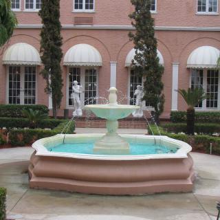 A decorative fountain surrounded by statues in a courtyard with a brick building backdrop.