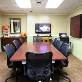 A well-equipped conference room with a large meeting table and office chairs facing a television.