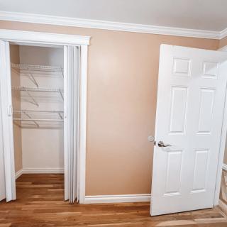 An empty room with a closet and open door, featuring wood flooring and beige walls.