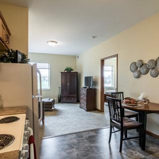 A cozy apartment interior featuring a kitchen area connected to a living space with dining furniture.