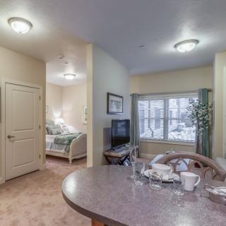 A cozy living space with a dining table, visible bedroom, and natural light coming through the window.