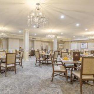 A spacious, elegantly decorated dining room featuring multiple tables and chairs under chandeliers.
