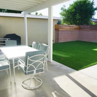 A sunny backyard patio with a table, chairs, grill, and a well-maintained lawn.