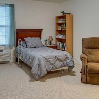 A cozy bedroom with a single bed, wooden bookshelf, and a comfortable armchair.