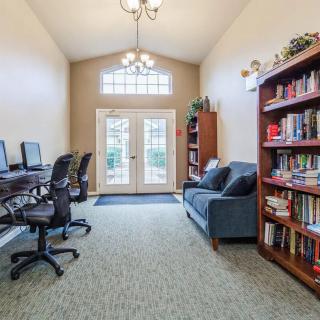 A cozy library room with computers, bookshelves, chairs, and a sofa.
