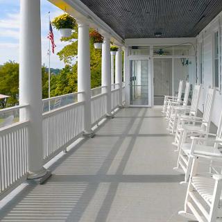 A serene view of a porch with white rocking chairs and columns.