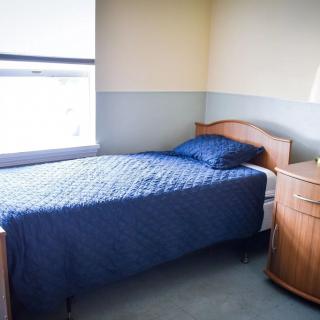 A simple bedroom with a single bed and blue bedding next to a window.