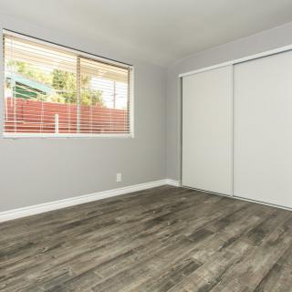 A simple, unfurnished room with laminate flooring and a window.