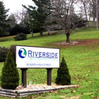 A welcoming sign for Riverside set against a green landscape.