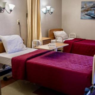 A hospital room with two neatly arranged twin beds, featuring red blankets and bedside tables.