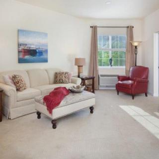 A cozy living room featuring a beige sofa, red armchair, and a large window providing natural light.