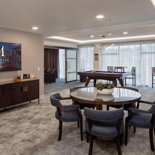 A modern living room featuring a dining table and a pool table, with elegant decor and a TV screen on the wall.