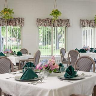 An elegant dining room with tables set for a meal, featuring folded napkins and floral centerpieces.