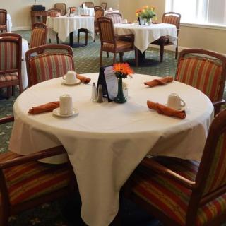 A neatly set dining table with a white tablecloth and orange napkins in a restaurant.