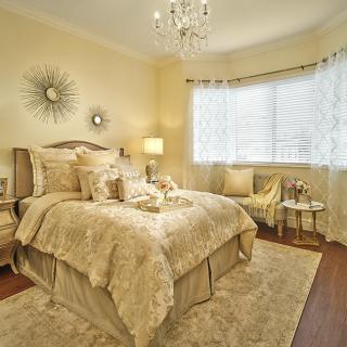A luxurious and elegantly decorated bedroom featuring a plush bed, chandelier, and warm lighting.