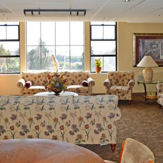 A cozy living room with floral patterned sofas, a coffee table, and large windows letting in natural light.