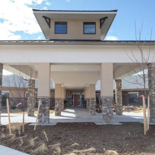 The image shows the entrance to a modern building with a covered walkway supported by stone columns.
