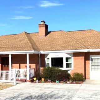 A single-story brick house with a porch and driveway under a clear blue sky.