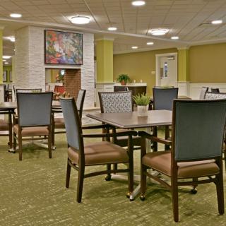A well-lit dining area featuring multiple tables and chairs arranged neatly on a carpeted floor.