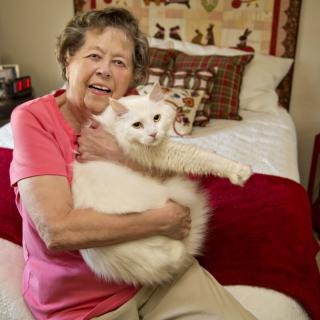 A woman smiling while holding a white cat in a cozy bedroom.