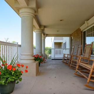 A spacious porch with columns, featuring rocking chairs and potted flowers.