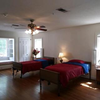 A spacious bedroom with two single beds, a ceiling fan, and natural lighting.