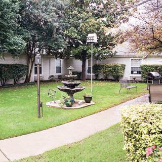 A tranquil garden featuring a central fountain surrounded by lush greenery and benches.