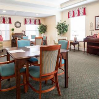 A cozy meeting room with tables, chairs, a piano, and natural lighting.