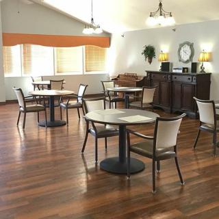 A cozy dining area with tables and chairs arranged on a hardwood floor, illuminated by stylish lamps.