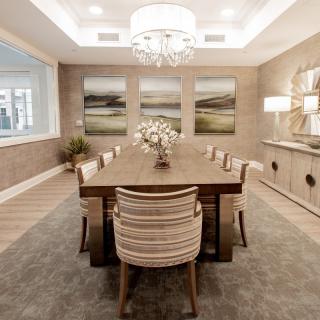 A modern dining room with a large wooden table, elegant chairs, and a chandelier overhead.