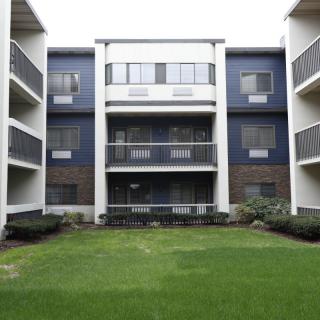 A modern apartment building with multiple balconies and a green lawn in front.