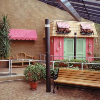 A charming indoor setting featuring a pink building facade with green shutters, benches, and a variety of potted plants.