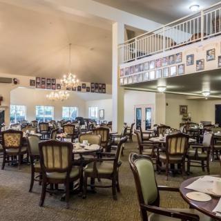 An elegant dining room with multiple tables and chairs, featuring a chandelier and balcony area.