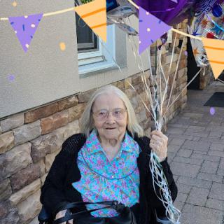 A joyful elderly woman celebrates with colorful balloons.
