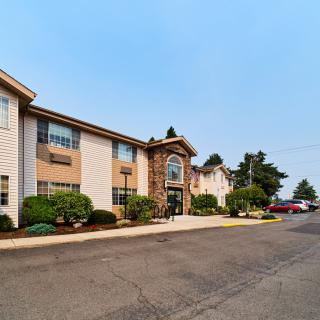 A two-story hotel building with a parking lot and landscaped entrance surrounded by trees.