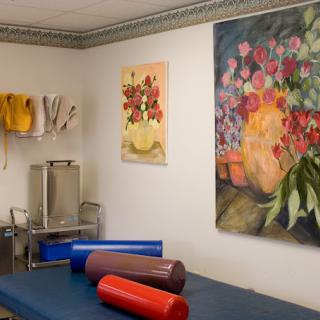 A therapy room featuring a massage table, colorful artwork on the walls, and various medical equipment.