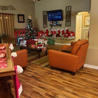 A cozy living room decorated for Christmas with a tree, presents, and stockings hung by the fireplace.