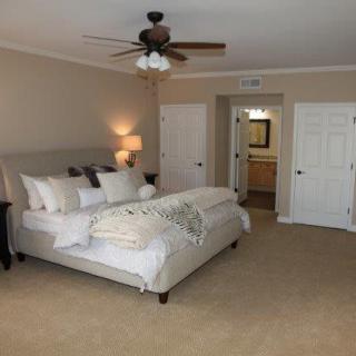 A cozy and spacious bedroom with a neatly made bed, carpeted floor, and a ceiling fan.