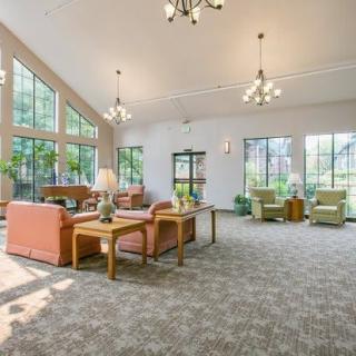 A spacious and bright living room with large windows, multiple sofas, and elegant chandeliers.