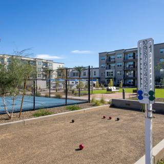 A modern apartment complex features an outdoor bocce ball court on a sunny day.
