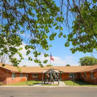 A brick building with a flagpole in front, surrounded by trees under a clear blue sky.